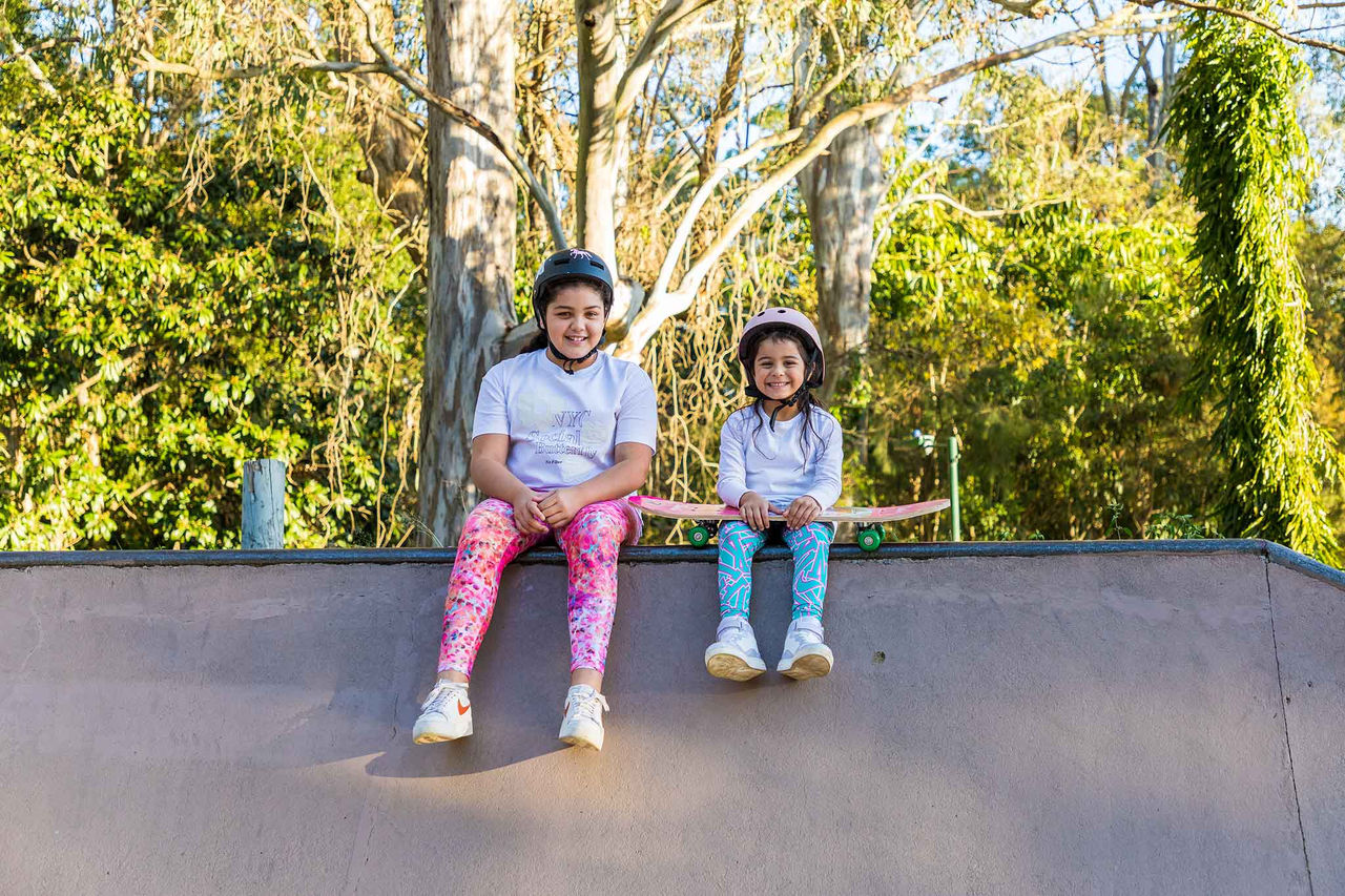 Two girls sitting on the skate park wall with helmets on at Hibiscus Skate Park.