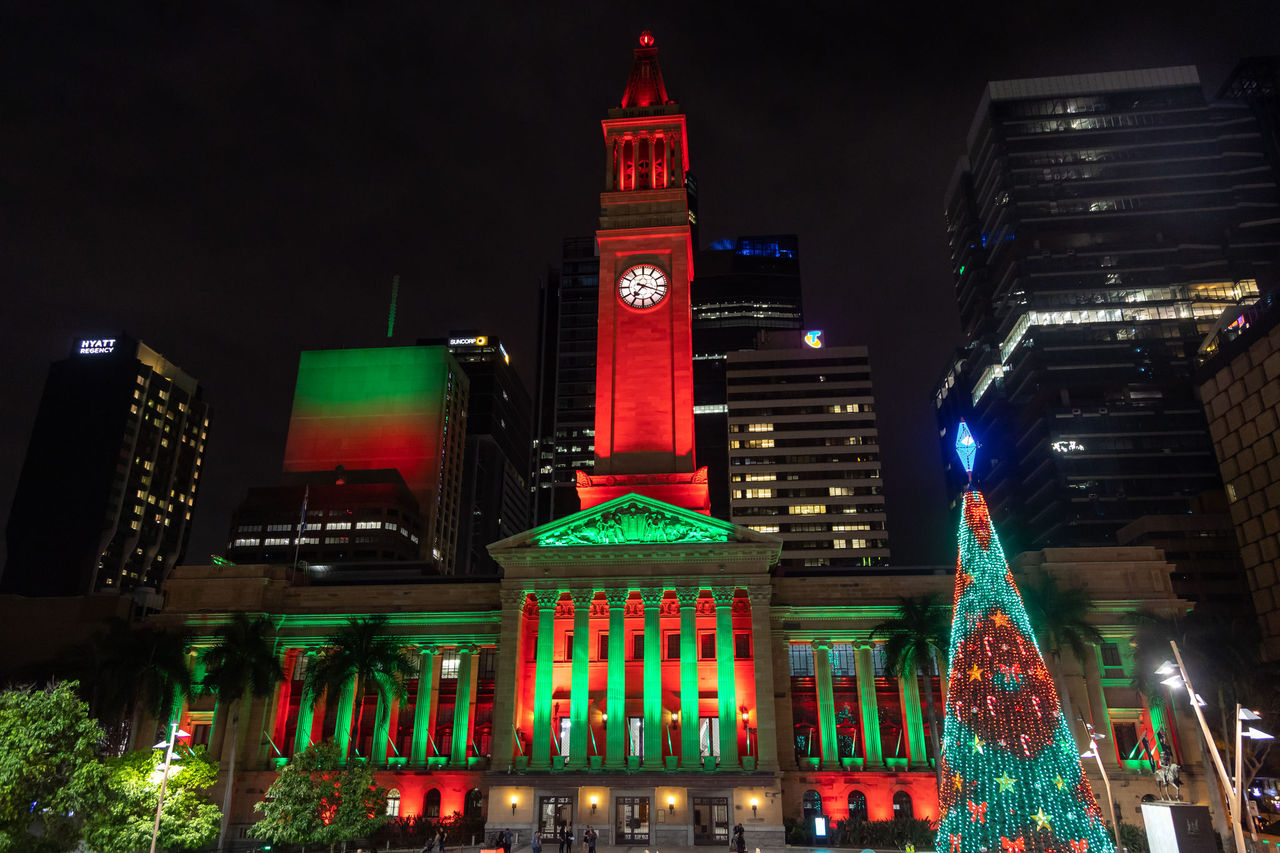 A Christmas tree in front of Brisbane City Hall with both lit up in green and red to celebrate Christmas.
