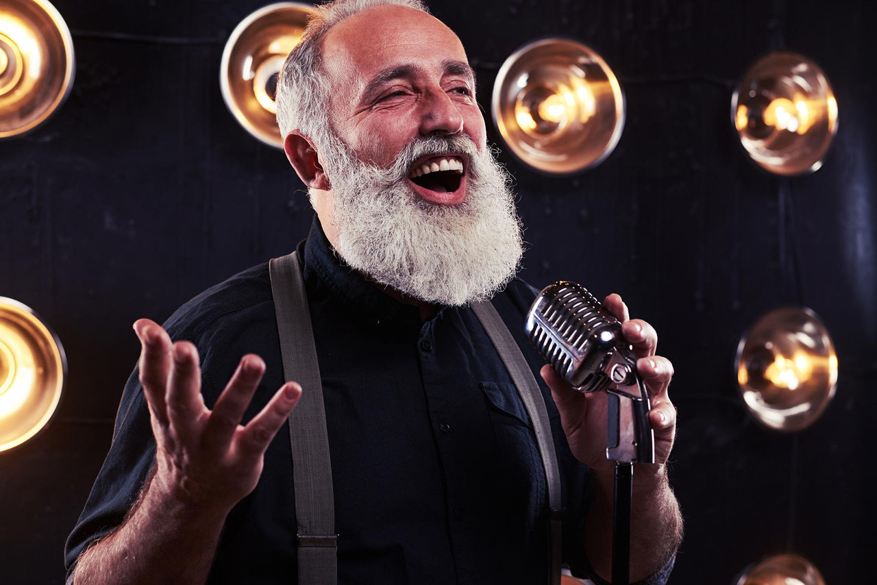 Senior male singing with cabaret-style mic in his left hand.