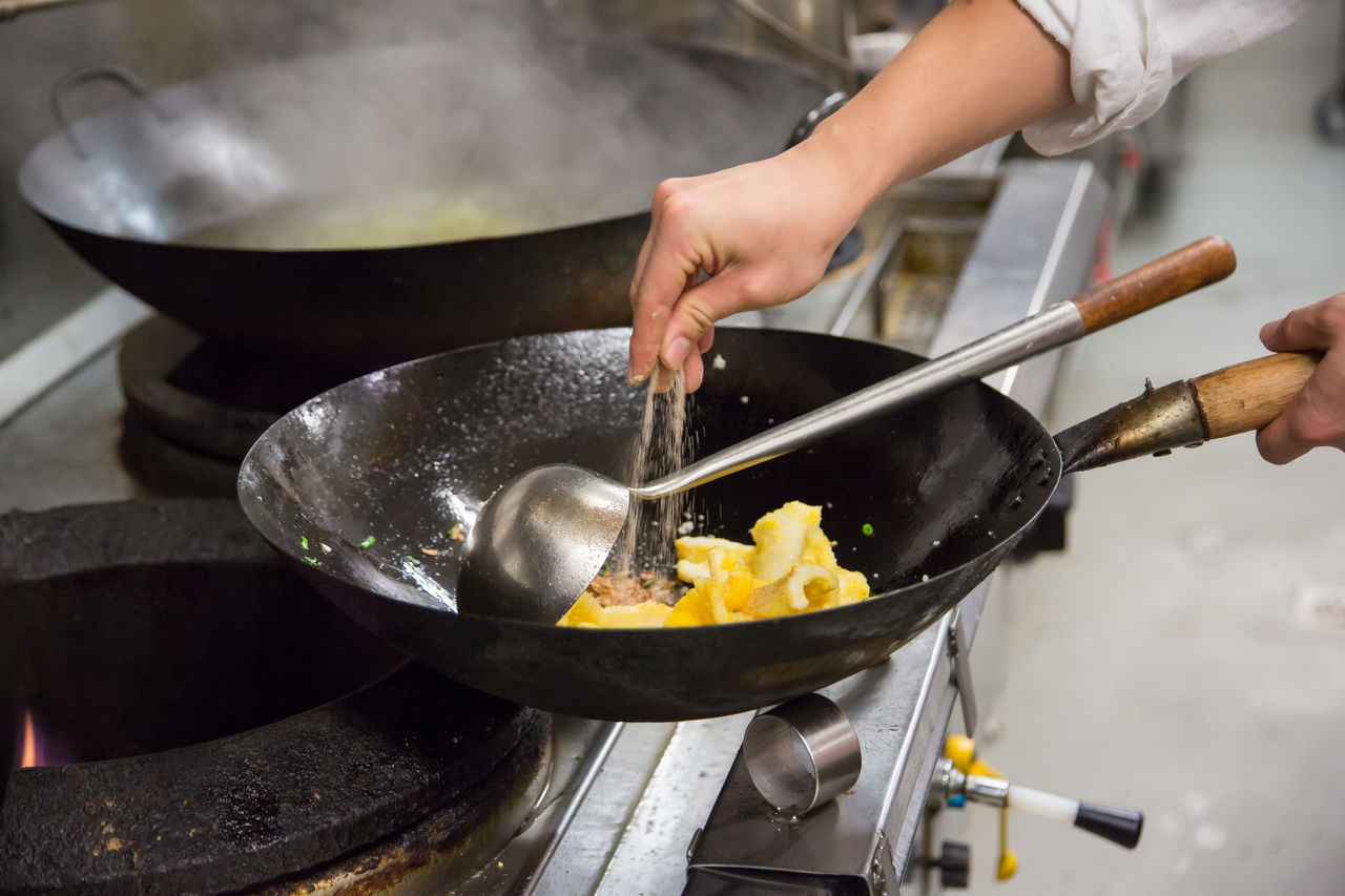 Close up of chef cooking in a commercial kitchen with pan and gas flame.