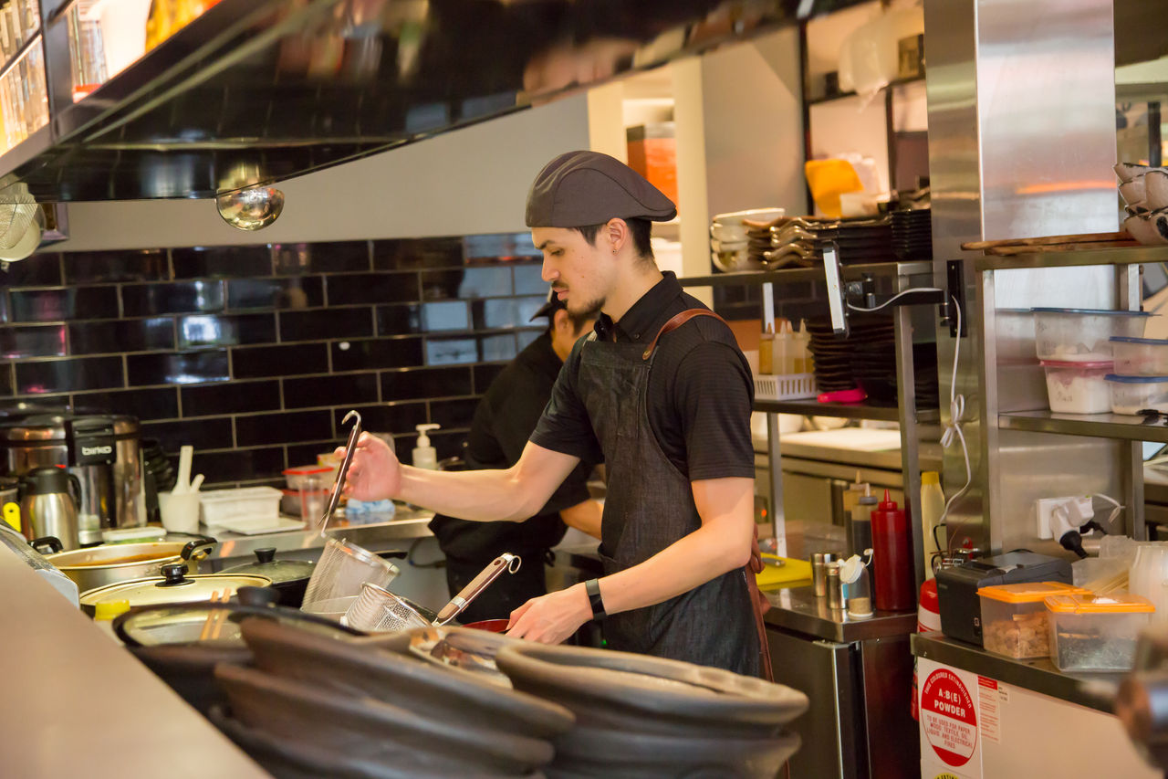 Male chef cooking over steamer and fryer in a commercial kitchen.