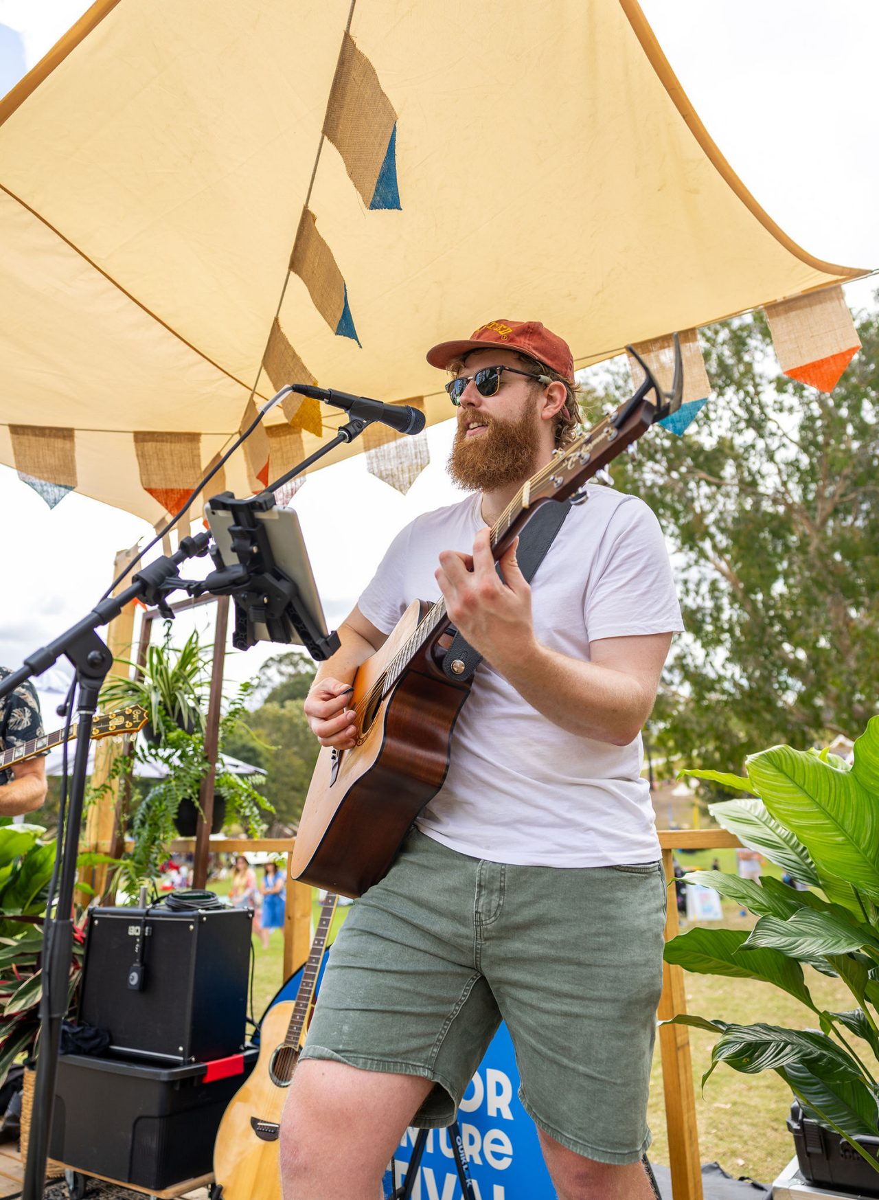 A man playing his guitar and singing into a microphone with sound equipment around him. 