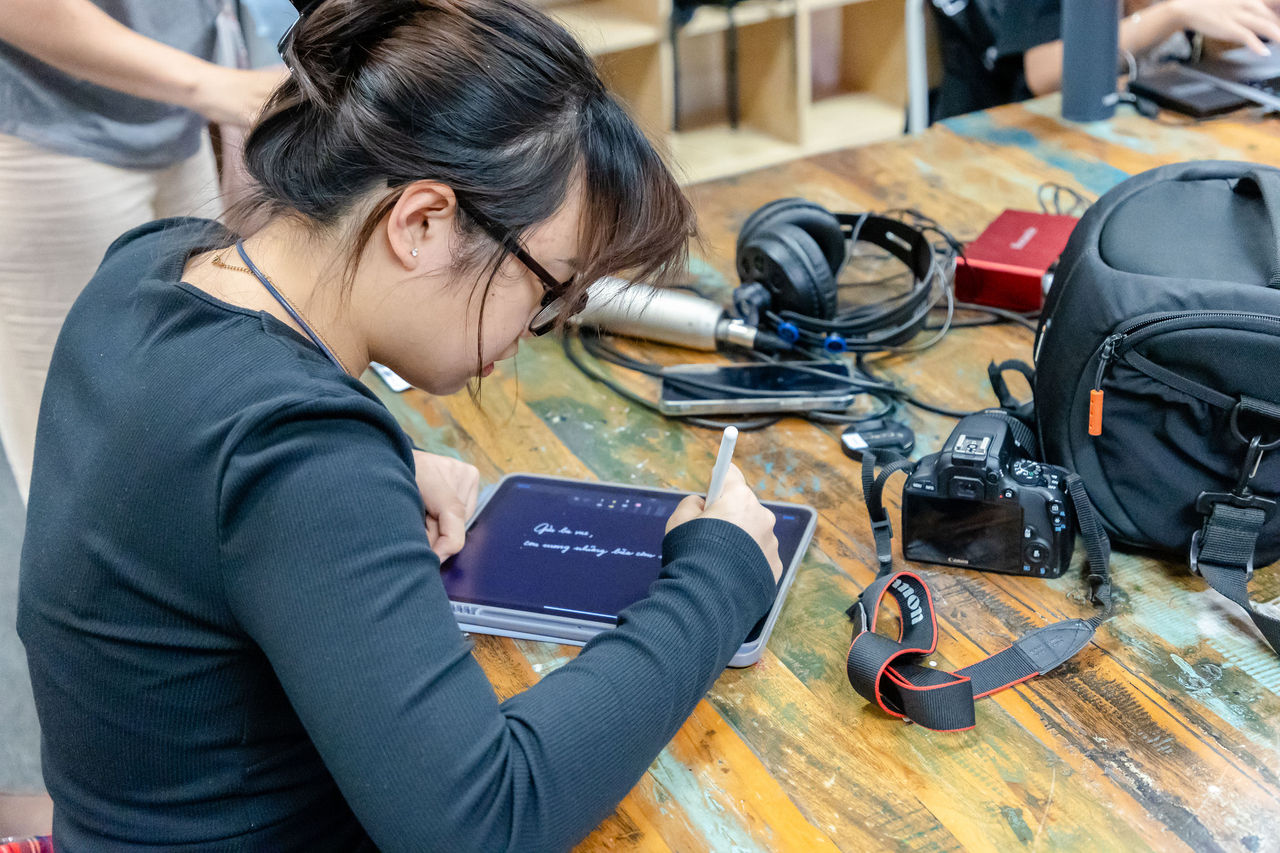 Young student filmaker with camera and sound equipment at Visible Ink. She's writing on a tablet.