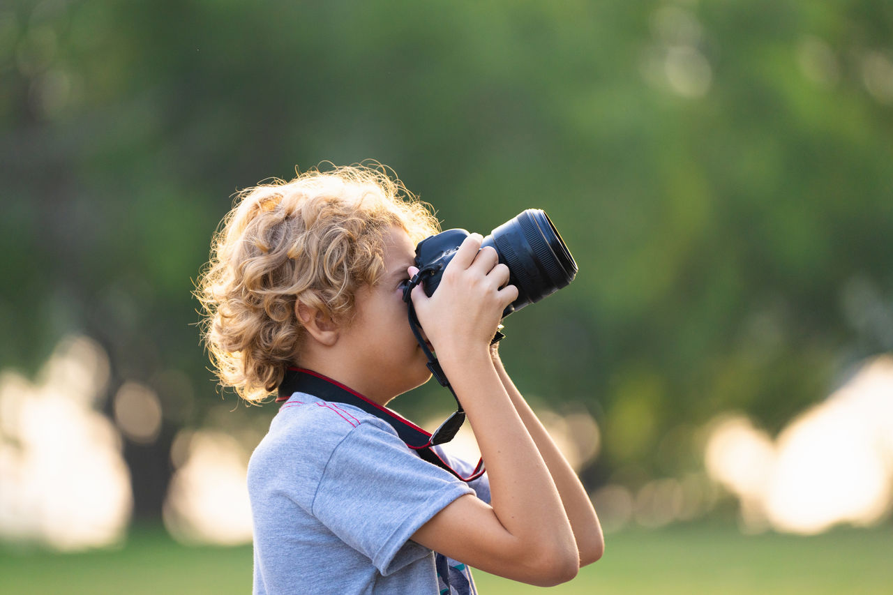 Child learning to take photos with a digital SLR camera in a natural setting.