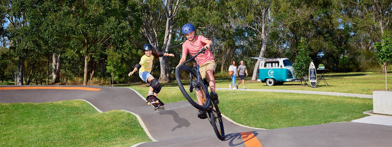 Two kids using the pump track at Mercer Park. The child in the foreground is riding a BMX bike and the child at the rear is using a skateboard.