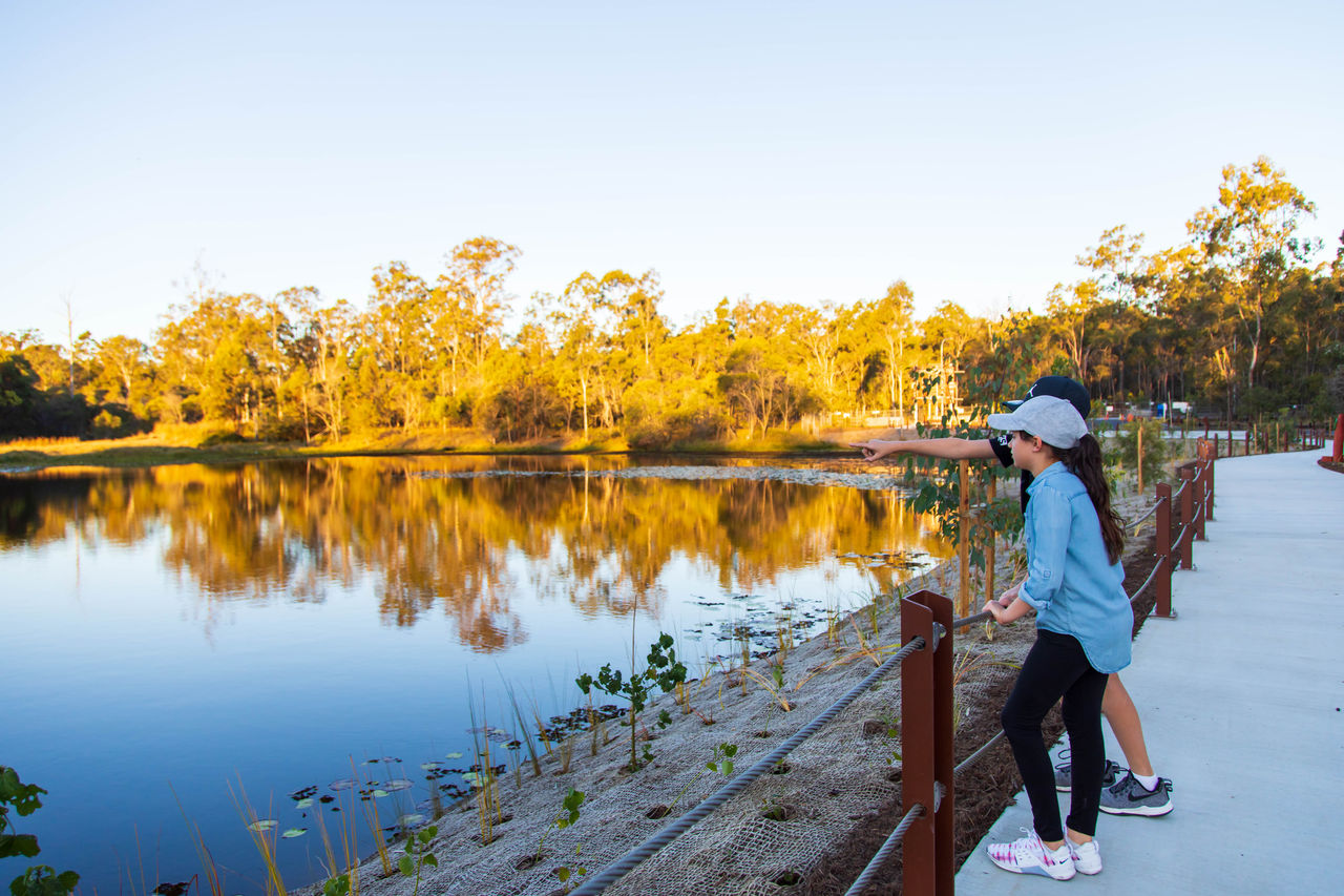 Two school-aged children dressed in casual clothing looking over Budela-budela Lake at Warril Parkland, Larapinta.