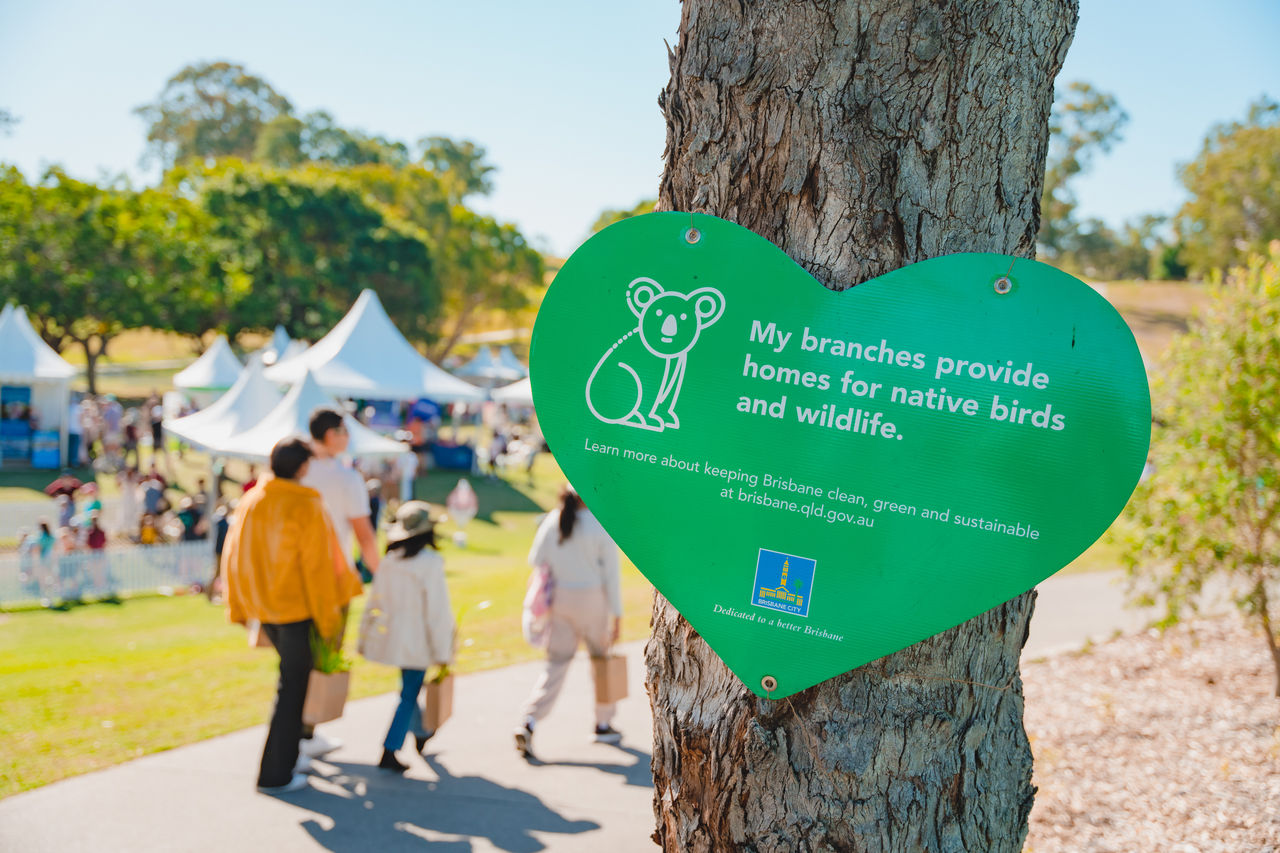 Love heart-shaped sign with a green background and  white text conveying a 'protect our native birds and wildlife' message at a Green Heart Fair at Victoria Park.