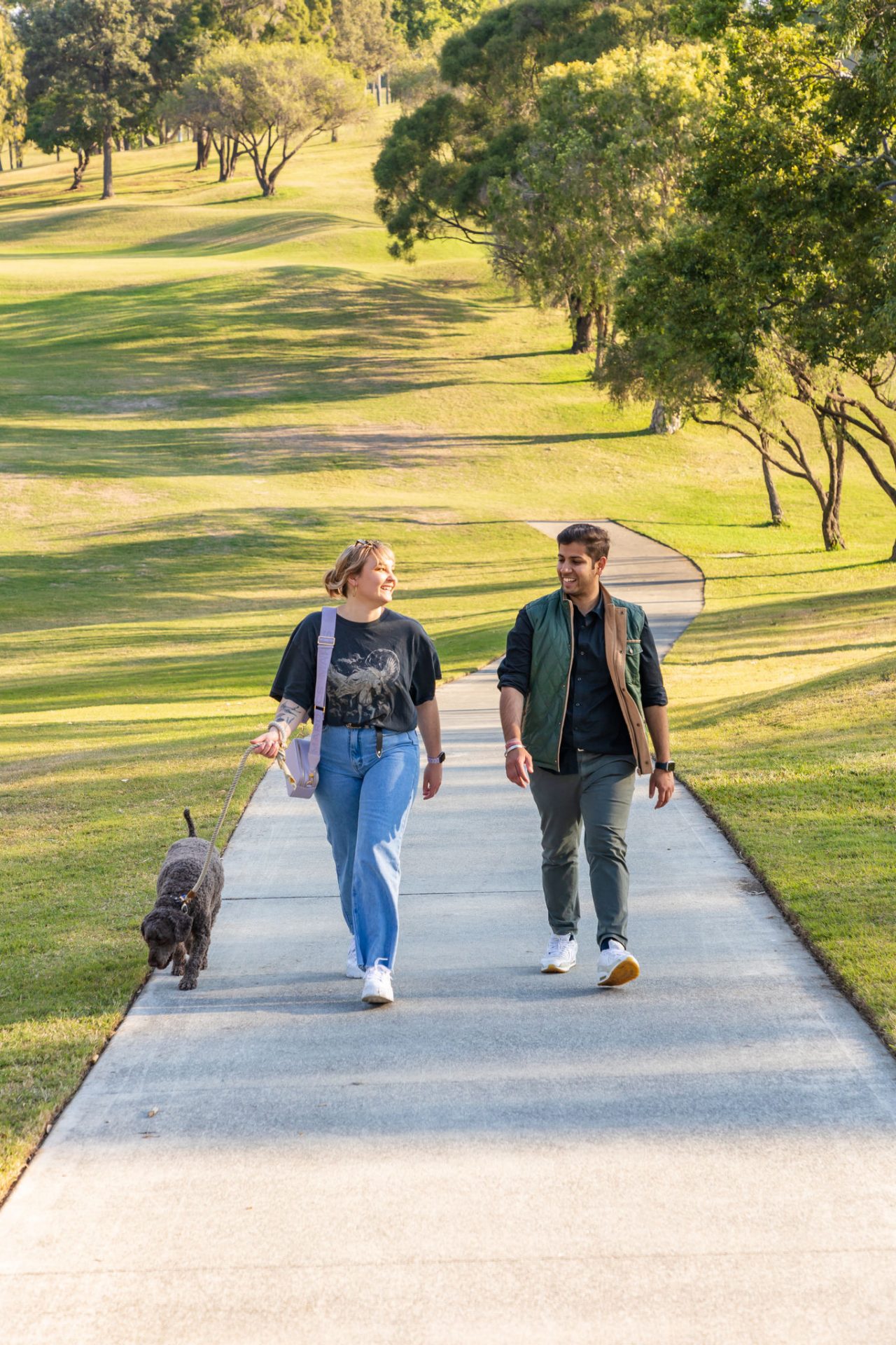A couple walking with a medium-size grey dog in Victoria Park.
