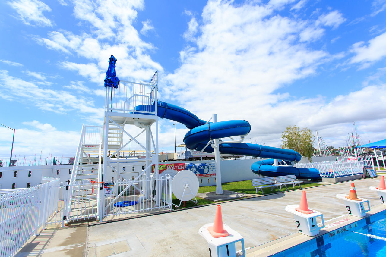 Image focus on waterslide structure at Manly Pool. Main outdoor pool with starting blocks in bottom right of image.