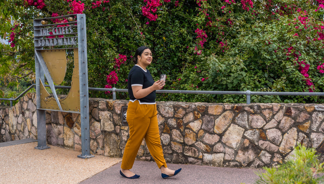 Young woman walking along The Cliffs Boarkwalk at Kangaroo Point. Smartphone in hand.
