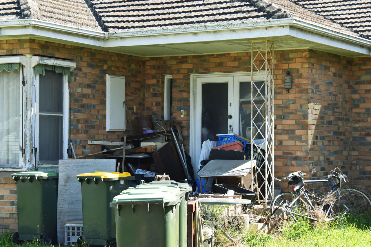 Unmaintained house with rubbish and clutter in front yard..