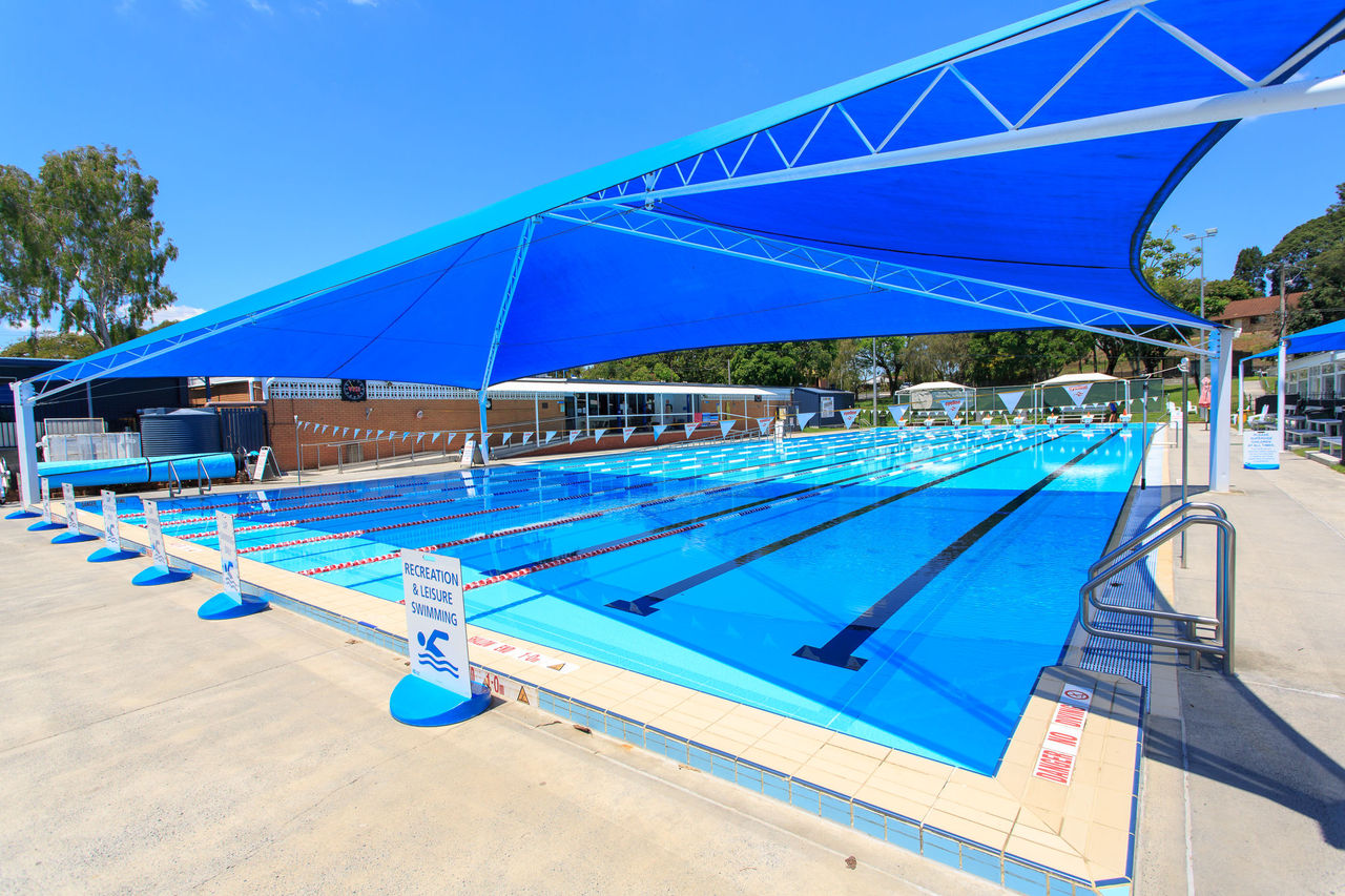 50 metre outdoor pool at Jindalee Pool. Image is taken from pool end with a shade structure across pool.