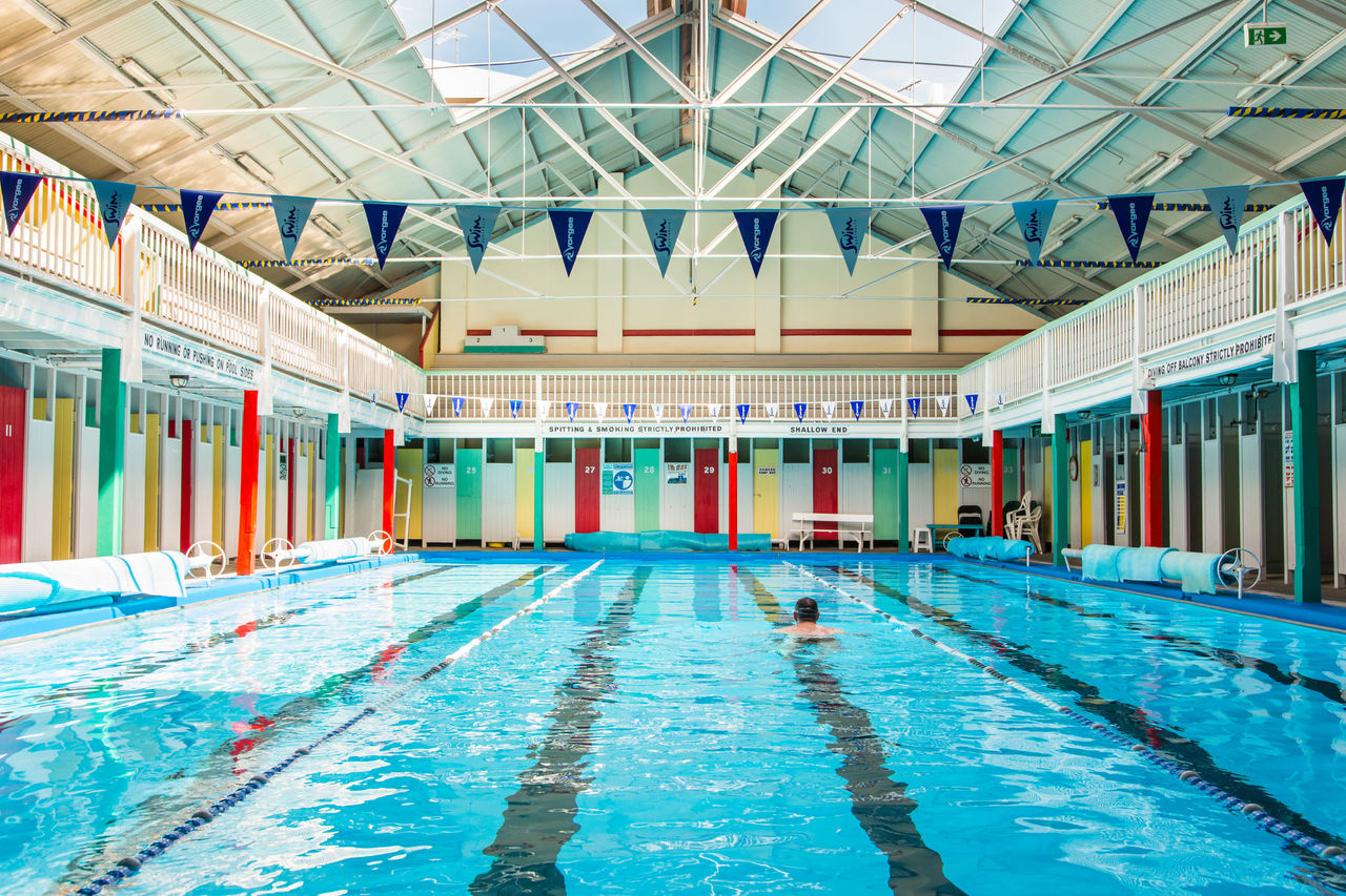 View of Spring Hill Baths pool with a swimmer in a middle lane. Roof of pool is open.
