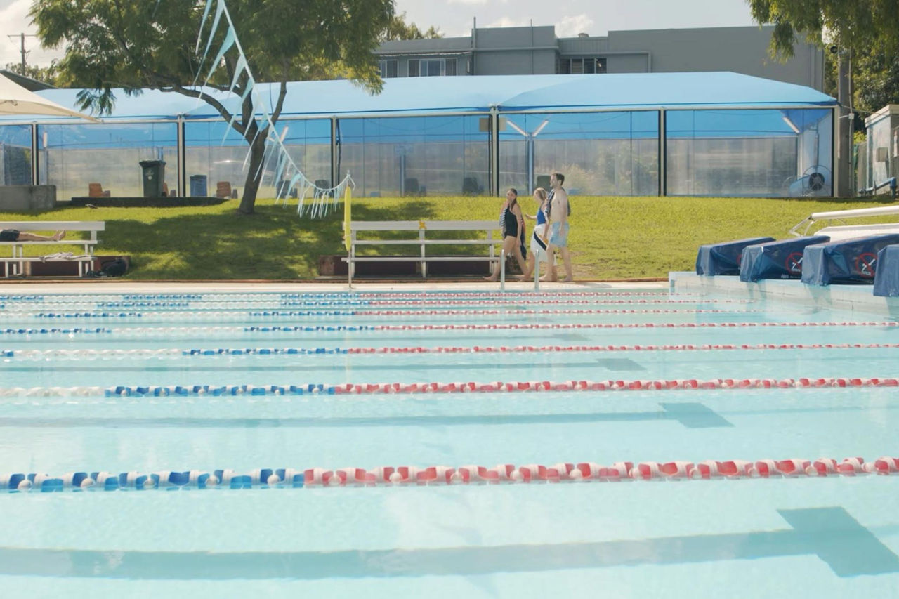 Three young people walking on far side of 50-metre pool at Hibiscus Sports Complex Pool