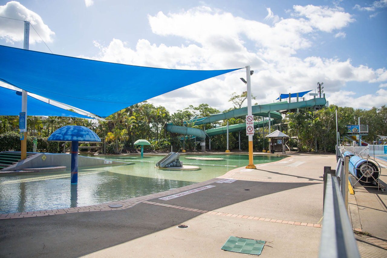Lagoon play area at Chermside Pool. Includes shade covers and water play equipment. Waterpark slide in background.