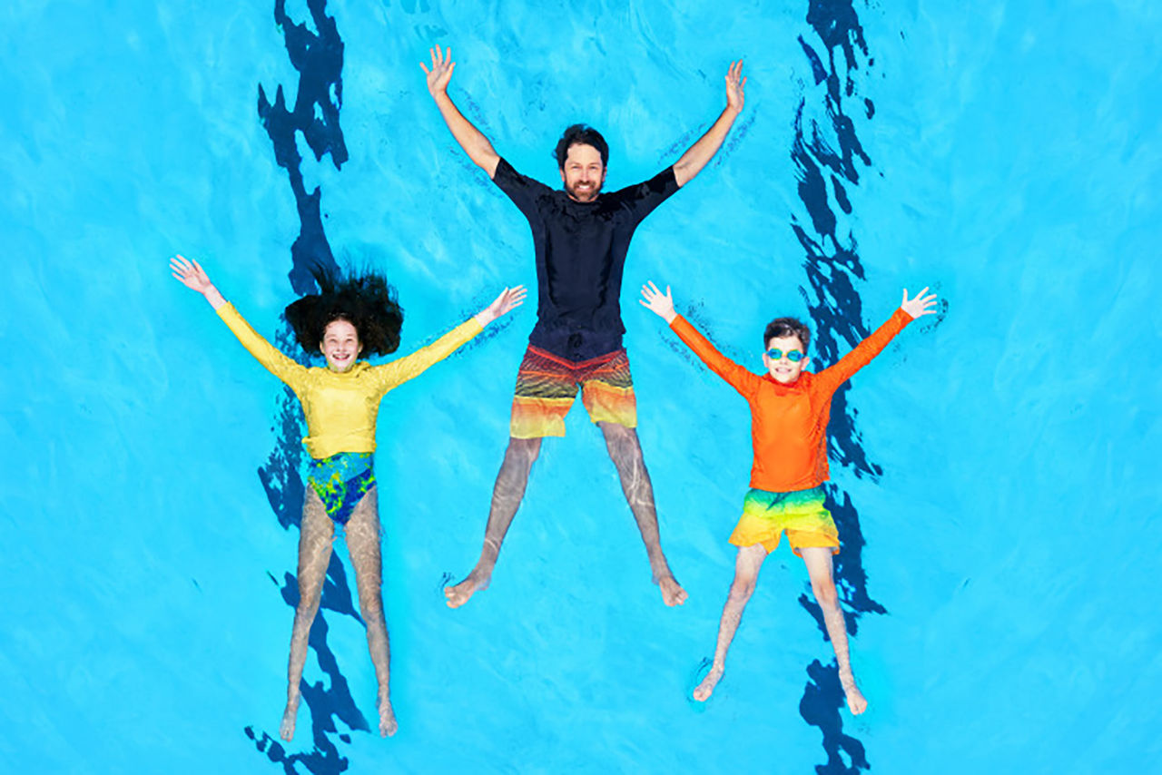 2 children and 1 adult floating in a pool with bodies displayed in a star shape configuration.