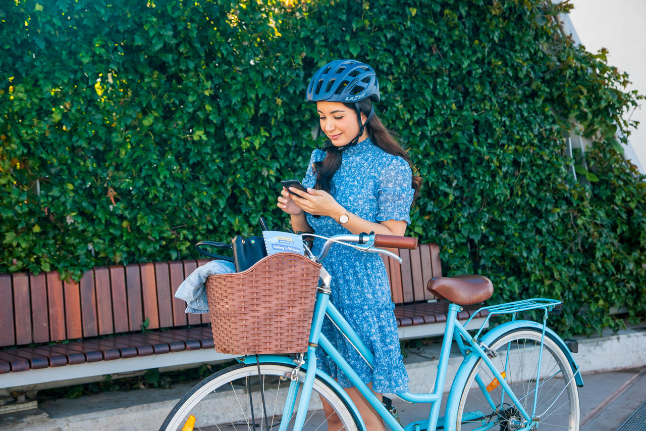 Woman standing beside a blue women's bicycle looking at smartphone at Bretts Wharf.