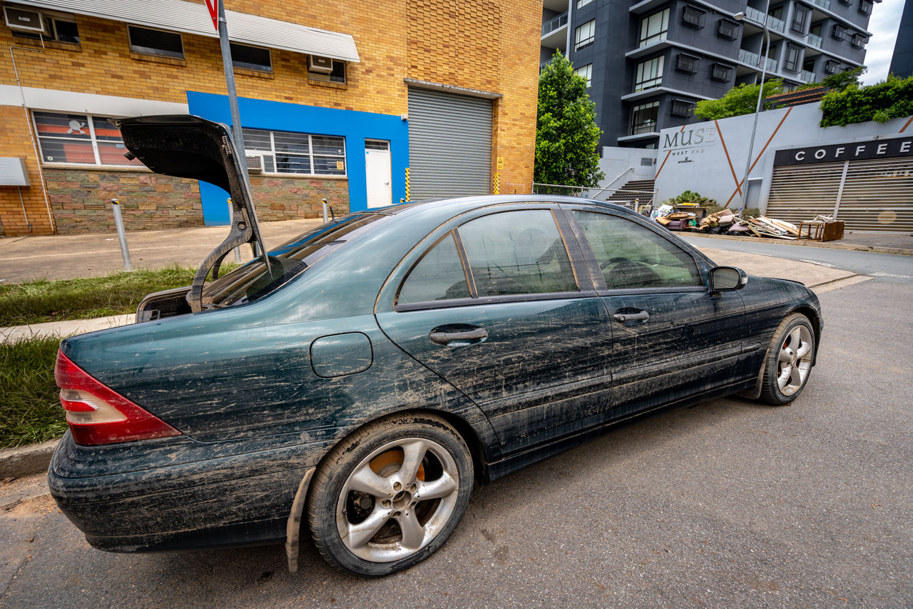 Green abandoned vehicle with boot open outside a commercial warehouse building on an inner Brisbane street.