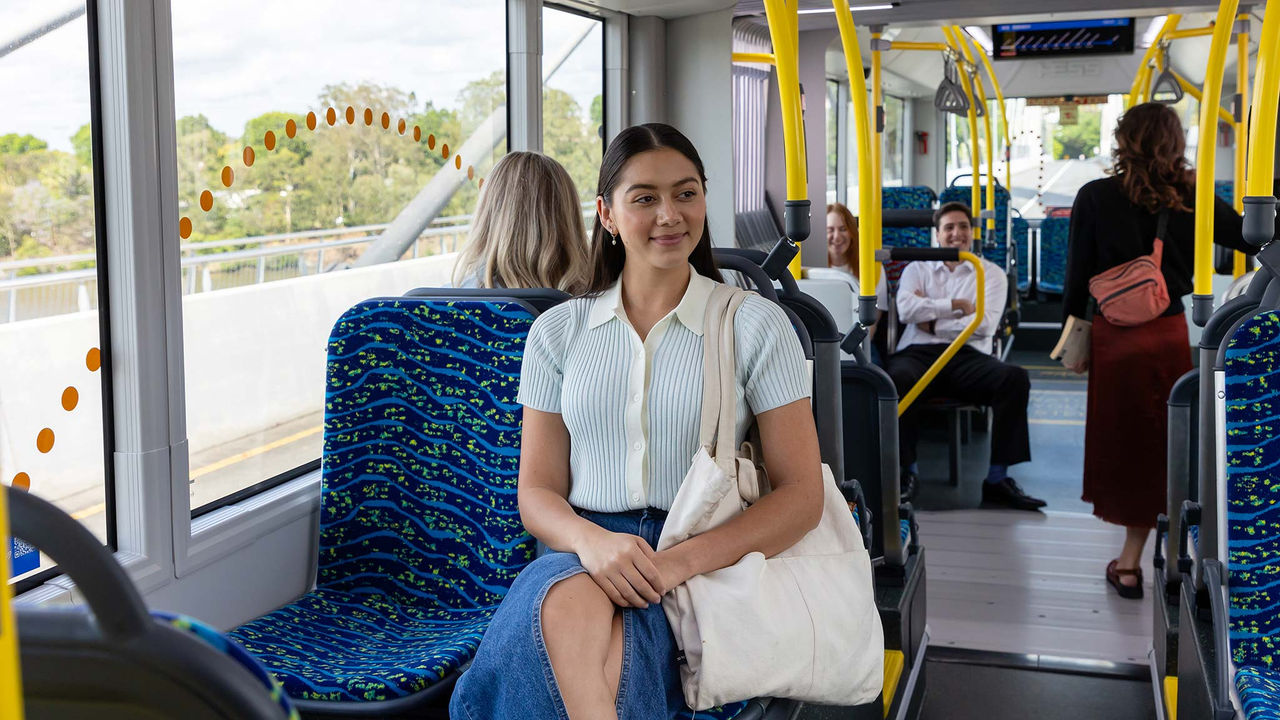 Female passenger sitting with crossed legs at front of metro. Other passengers in background.