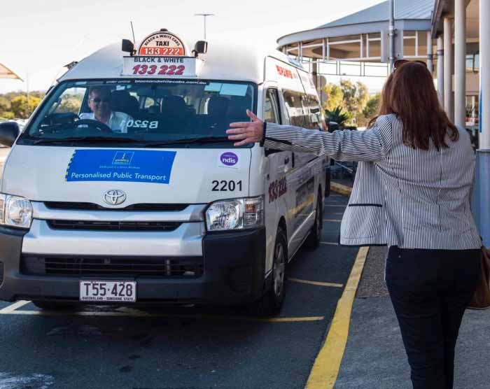 Woman hailing a Black & White taxi which is badged with a branded Council Personalised Public Transport sign.