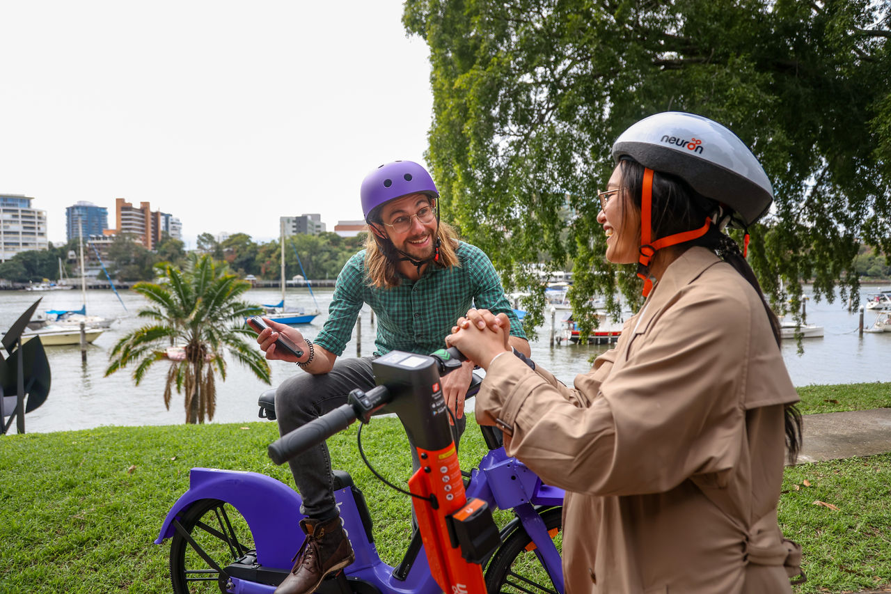 Man using a Beam electric bike talking with a woman using a Neuron electric scooter.