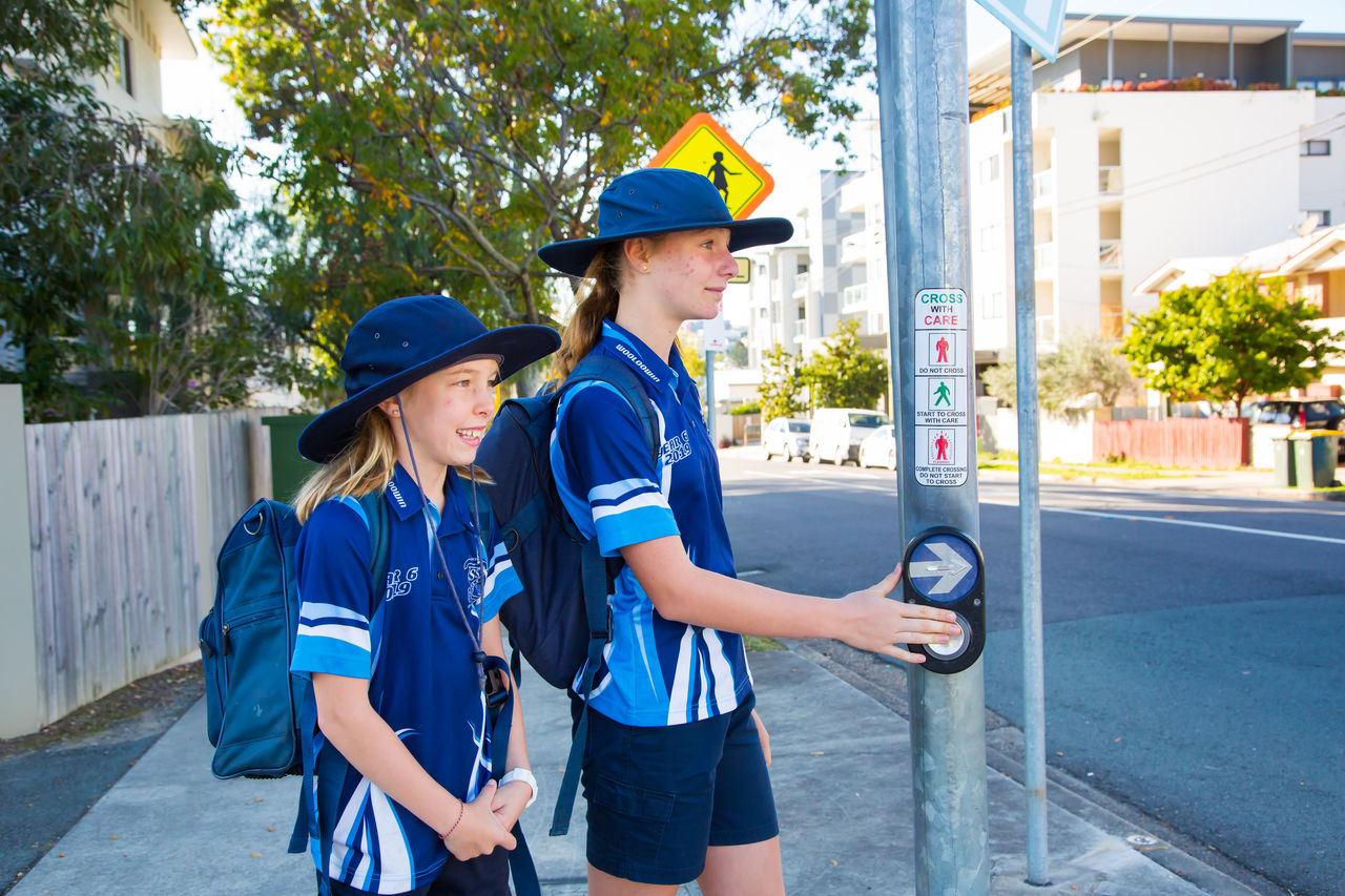 2 female Wooloowin State School middle school students walking to school. Standing at a crossing.