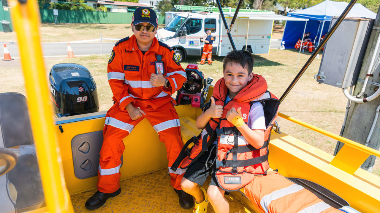 State Emergency Services volunteer in orange uniform sitting with a child wearing a lifejacket.