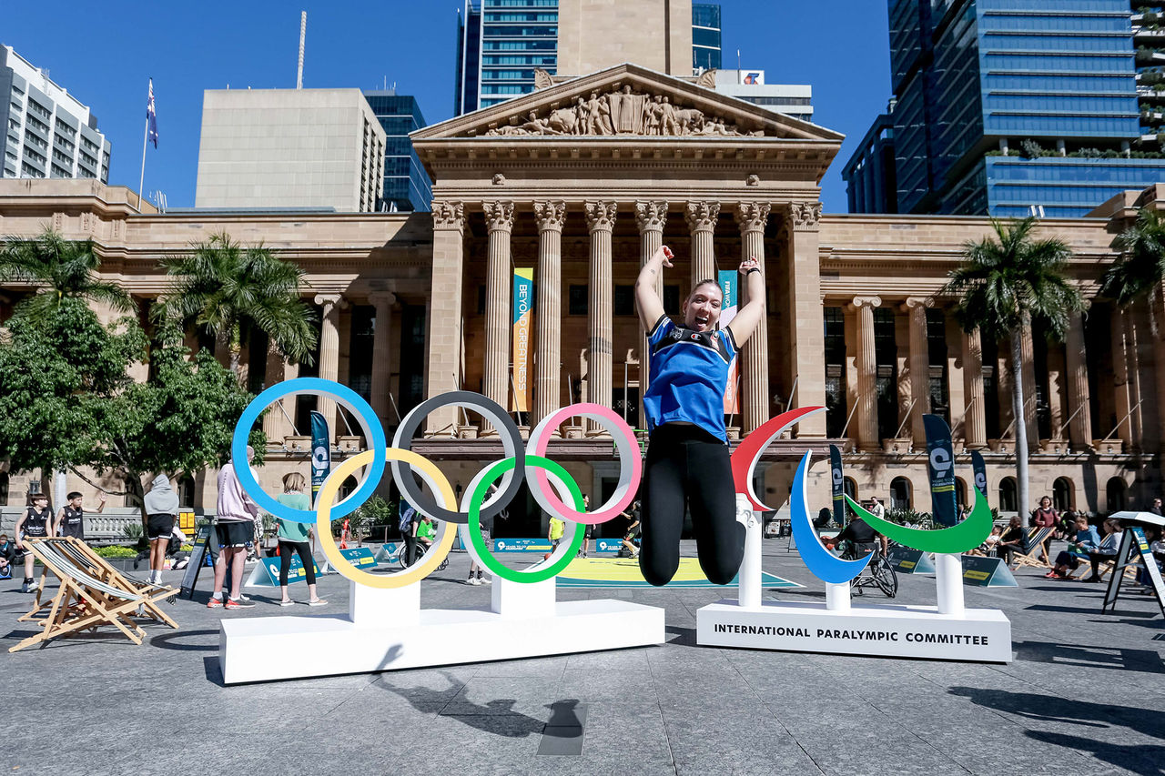 Brisbane City Hall Olympics activation with woman jumping cheerfully in front of the Olympic Rings and Paralympic Agitos