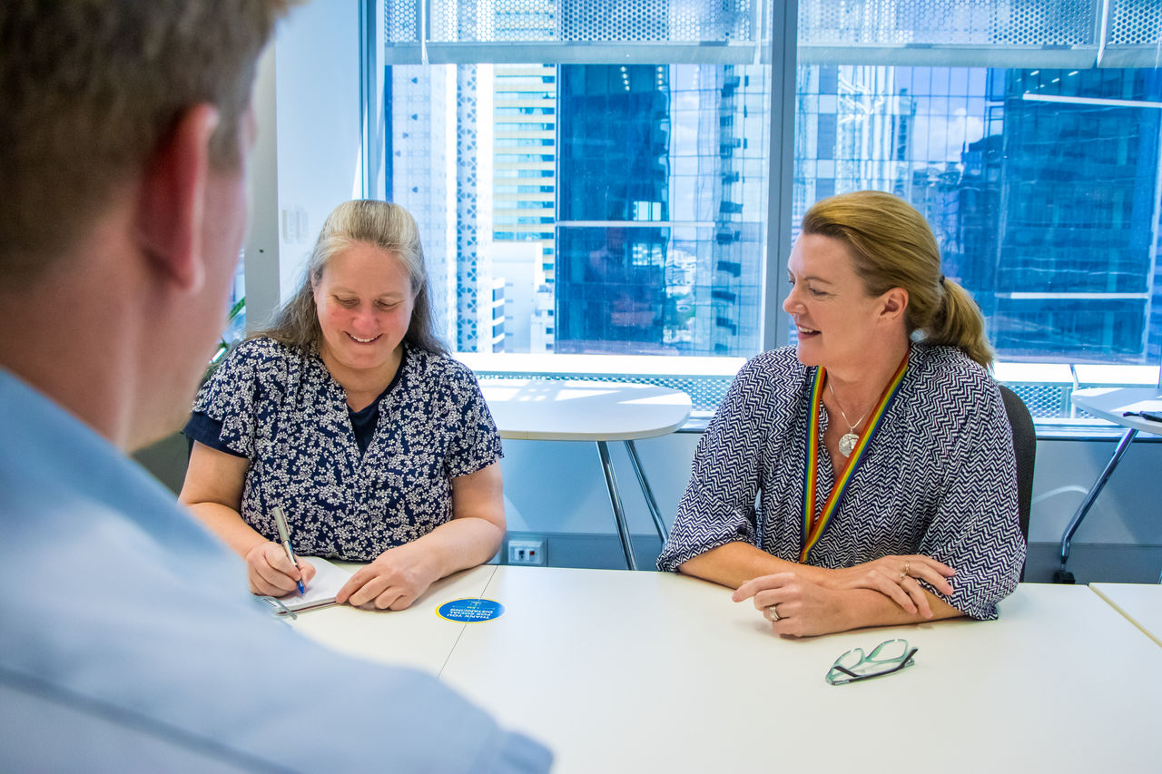 Three Council office-based staff in discussion in a meeting room with cityscape in background.