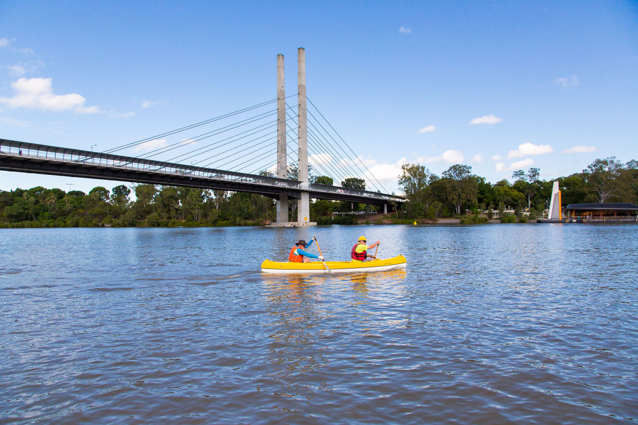 Two people in a tandem kayak on the Brisbane River at Dutton Park with the Eleanor Schonell Bridge in the background.