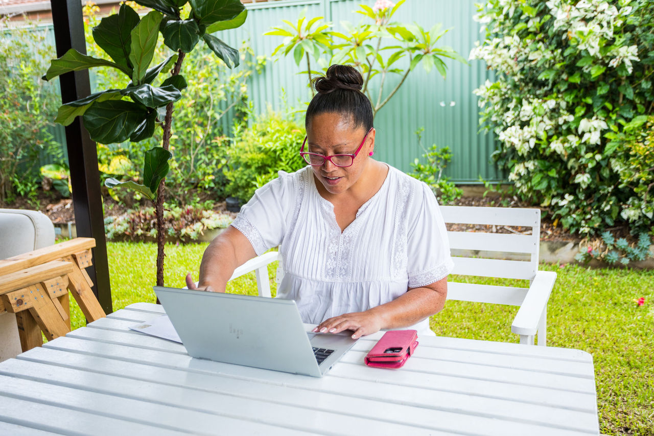 Woman sitting at an outdoor table with a laptop and phone.