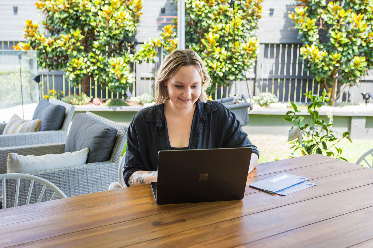 Woman using a laptop on a outside table in a home setting.