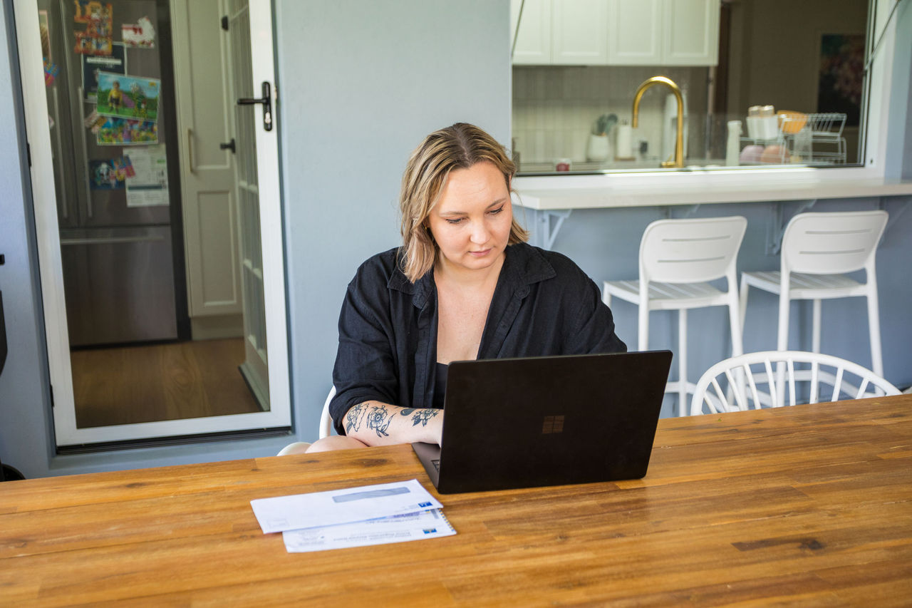 Woman sitting at an outdoor table working on a laptop. Council bills sitting beside her.