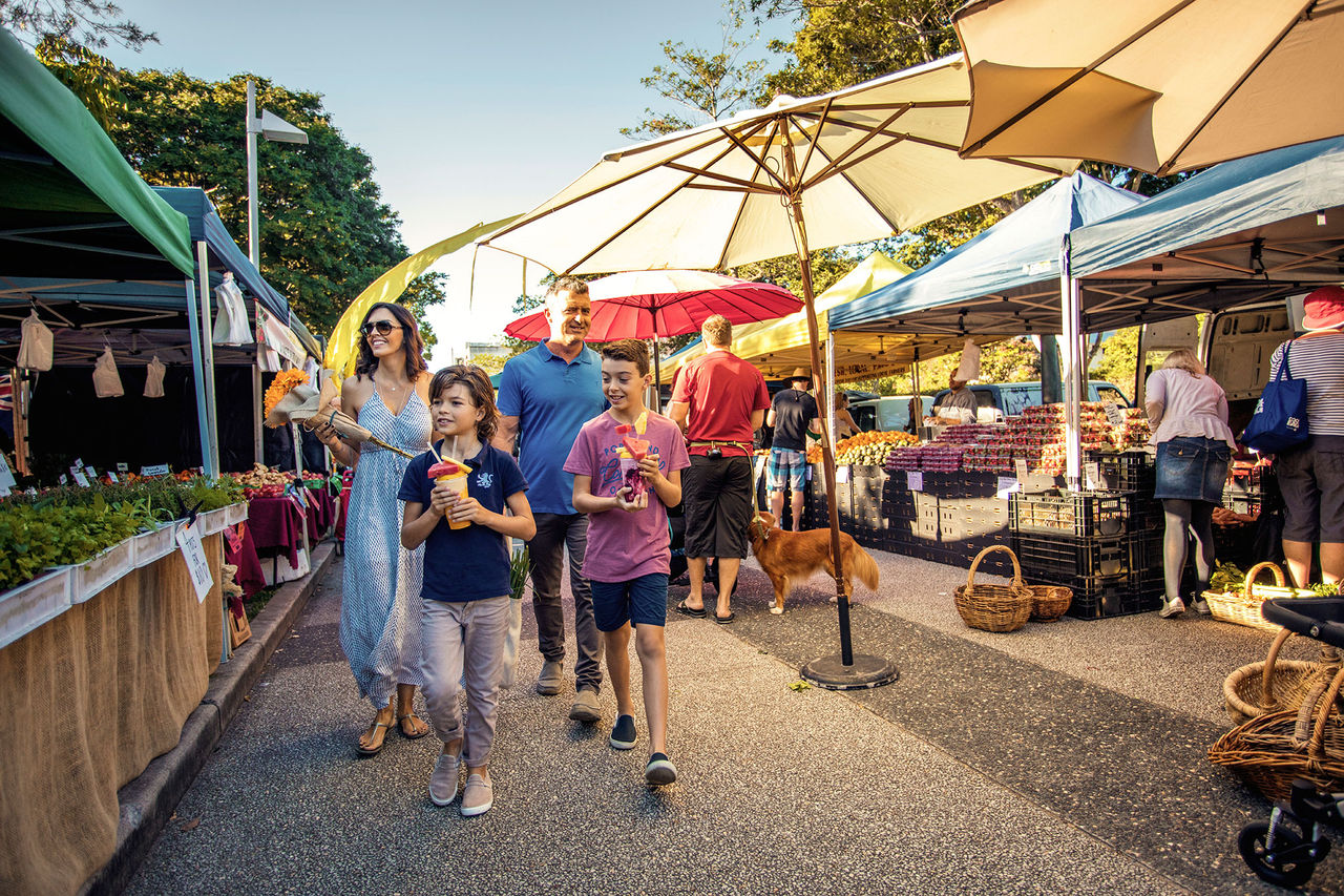 A family walking through market stalls at the Brisbane Powerhouse markets at New Farm