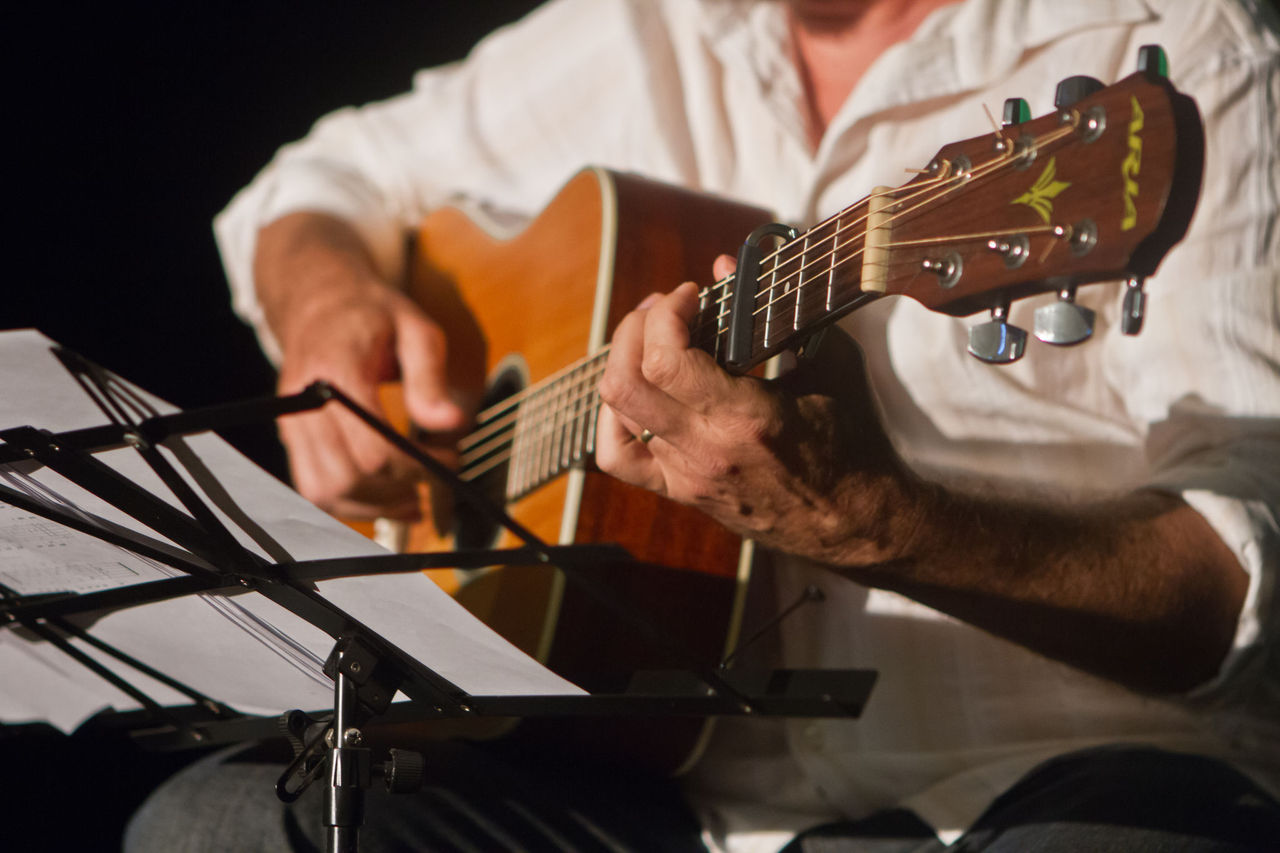 A close-up image of the mid-section of a man playinig acoustic guitar with music stand and sheet music at Sandgate Town Hall.