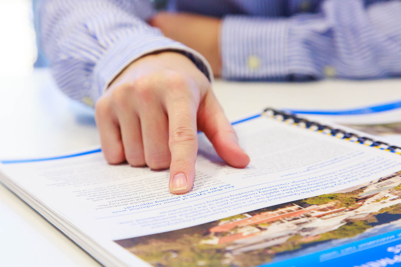 Close-up of a man's hand with index finger pointing to a bound document on the desk.