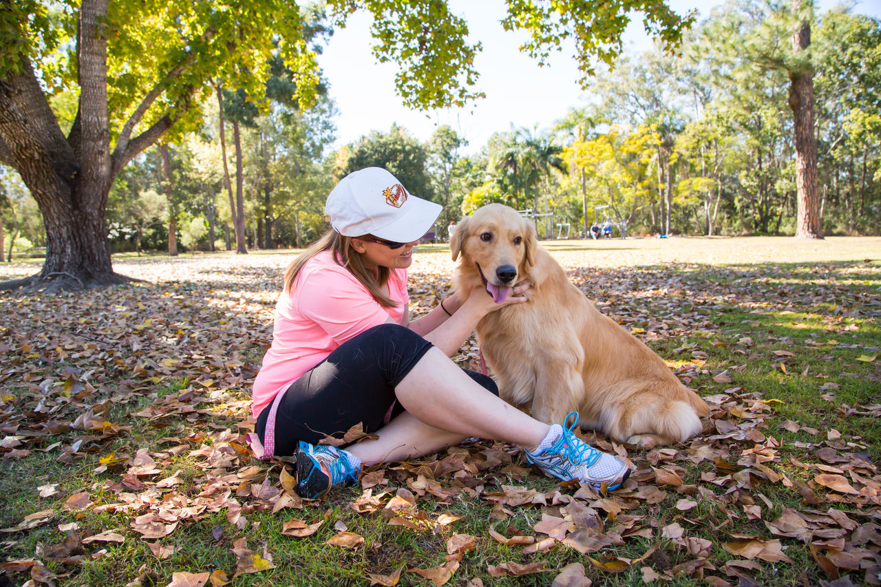 Woman in activewear sitting cross-legged in a Brisbane dog park with a yellow Labrador by her side.