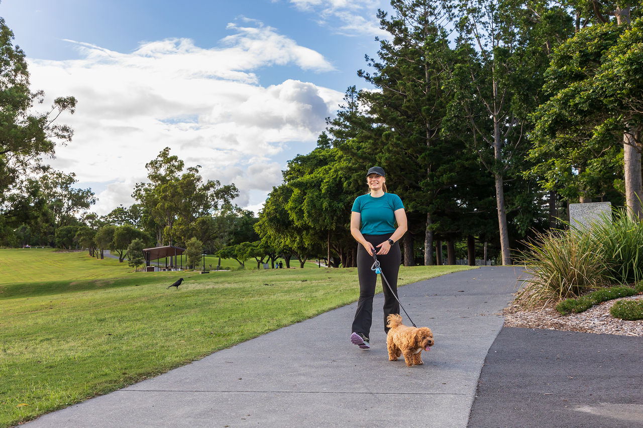 Woman walking a small, brown, curly-haired dog on a lead in Victoria Park.