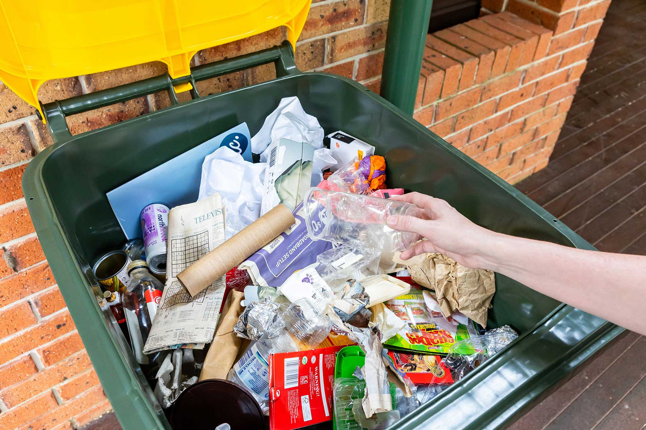 Recyclable items being placed into a recycling bin which has cardboard and other items in the bin.