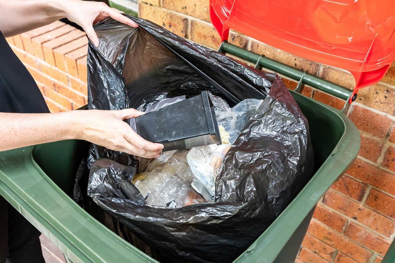 General waste items being placed into a red lidded bin.
