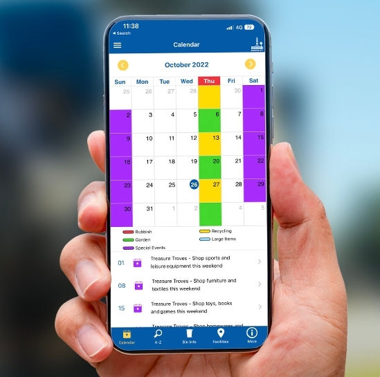 Hand holding smartphone displaying Bin and Recycling app with calendar.