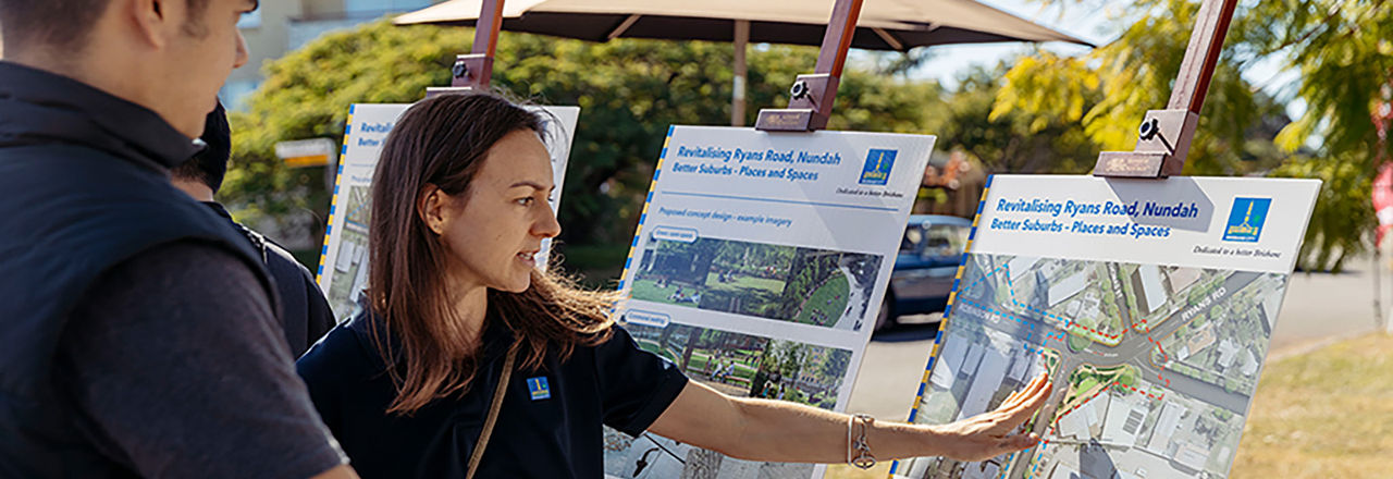 A man standing with a female Council officer looking at easels with the proposed concept design plans and imagery for Ryans Road, Nundah.