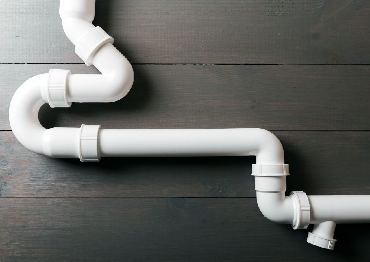 White plumbing pipes on a dark brown, wood background.