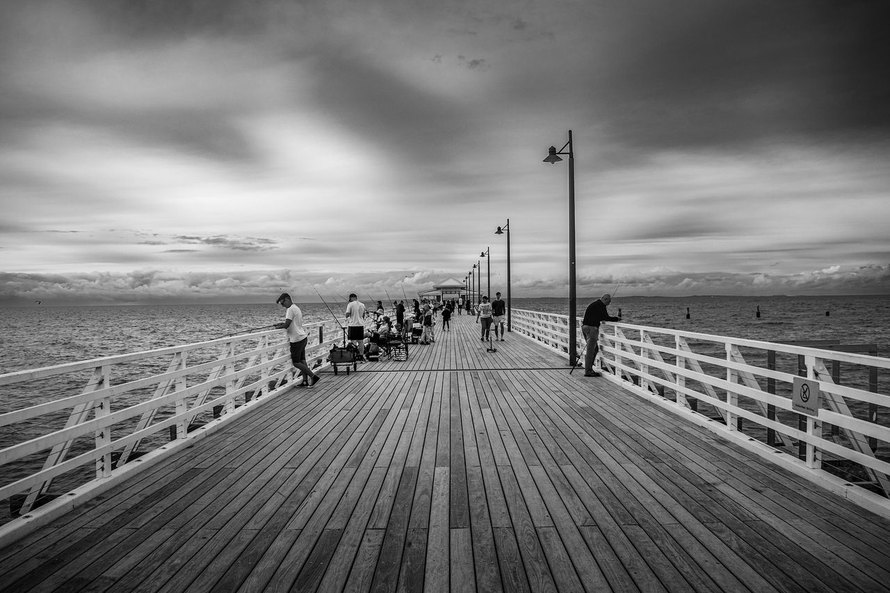 LMPA-2026-Peoples-Choice-Finalist-Lyle-K-Tight-Lines. A black and white image looking down Shorncliffe Pier with people fishing on either side.
