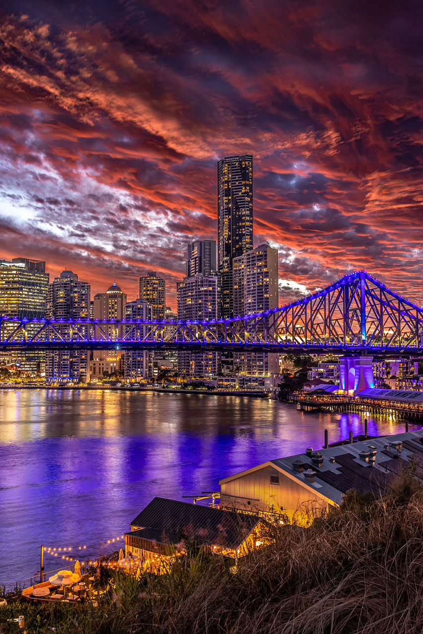 LMPA 2026 Peoples Choice Finalist - Ziwen Qu - When Brisbane Burned Gold and Crimson. The Story Bridge lit up in blue with a gold and crimson cloudy sky behind.