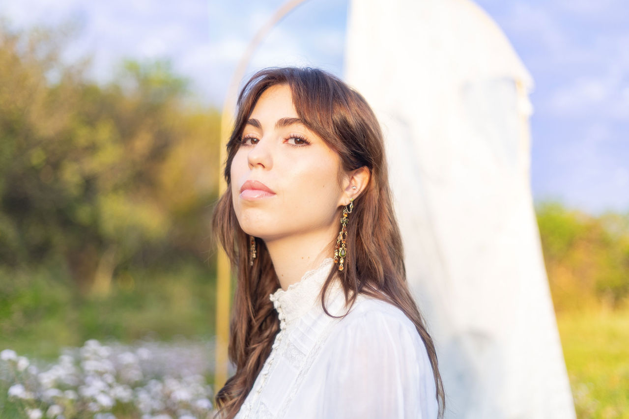 Georgia Scarlett - finalist in The QUBE Effect 2026 - standing in a field with trees and flowers.
