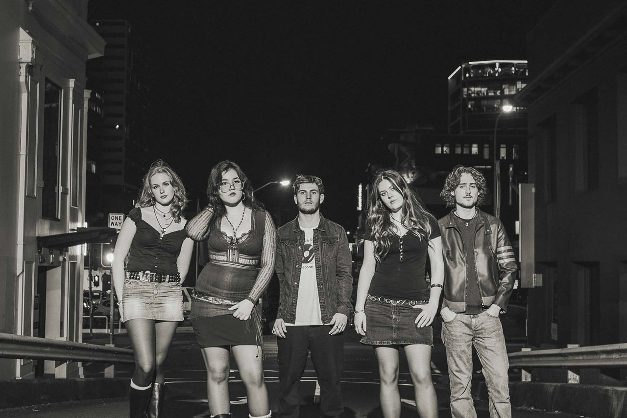 Hyphen band members - finalists in The QUBE Effect 2026 - in a black and white image shot at night with cityscape in background.