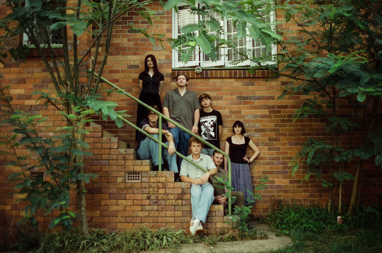 Still Full From Lunch band members - finalists in The QUBE Effect 2026. Photographed on the front steps of a brick postwar house.