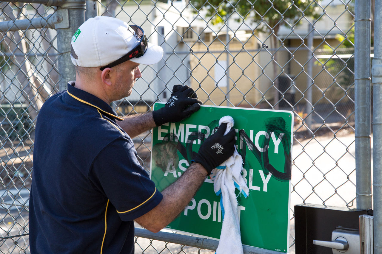 Council officer removing graffiti from an 'emergecy assembly point' sign.