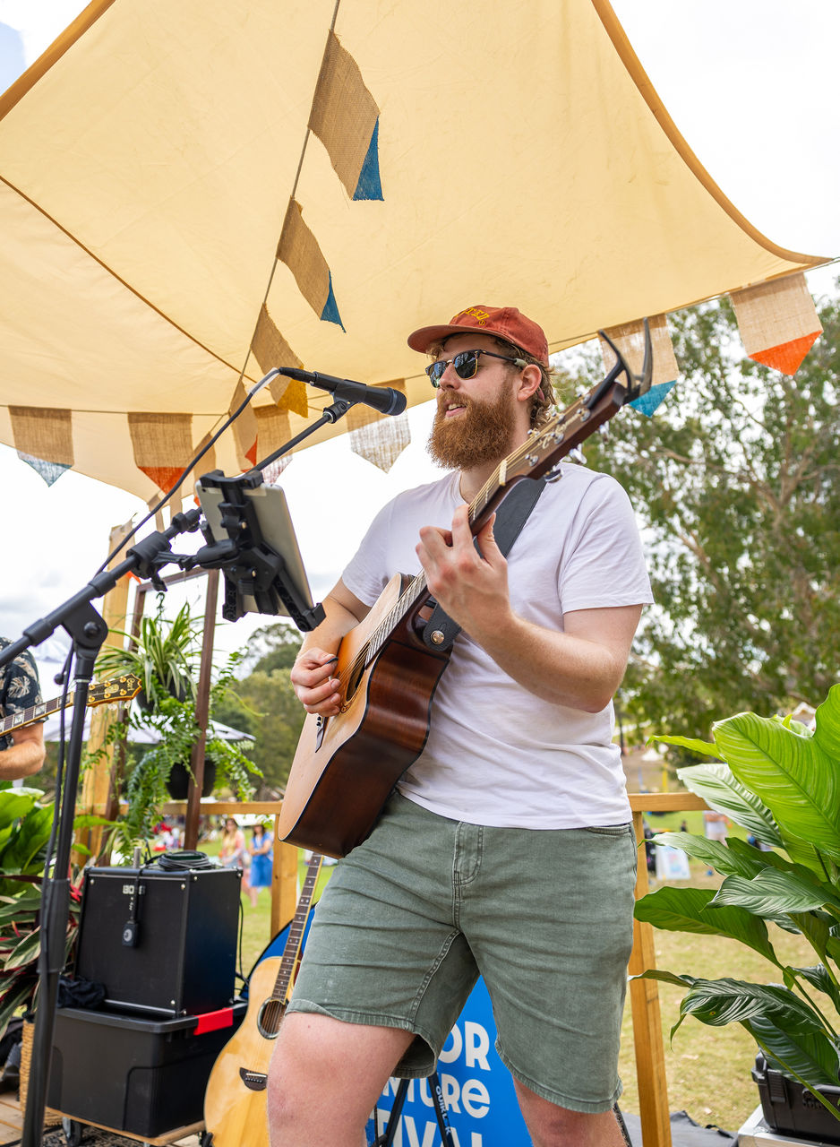 A person playing his guitar and singing into a microphone with sound equipment around him. 